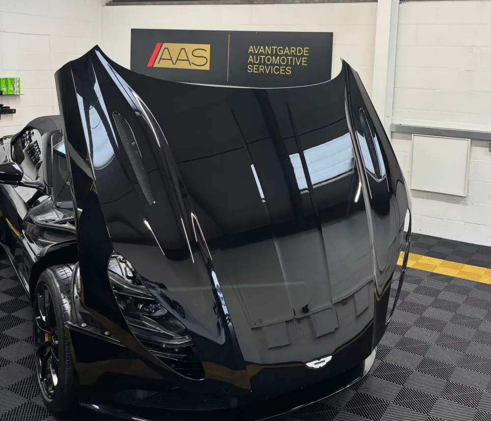 Black Aston Martin with its bonnet raised inside the Avantgarde unit, under the company sign